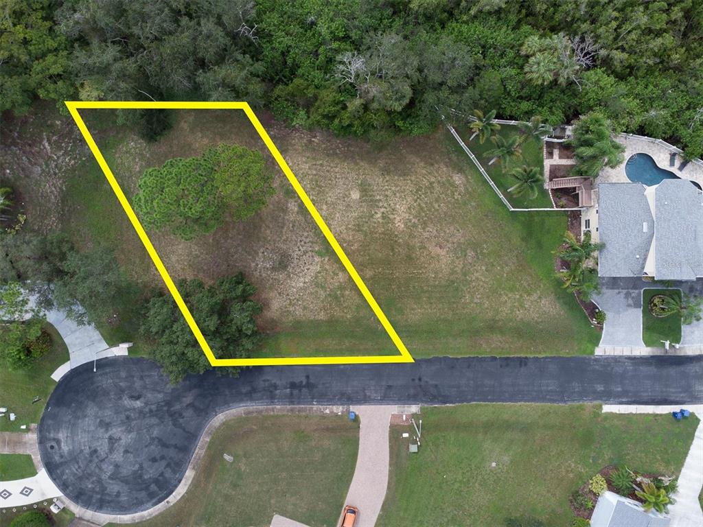 An aerial view shows a vacant residential lot outlined in yellow near a coastal forest — 3034 SHEPPARDS CROOK, HOLIDAY, FL