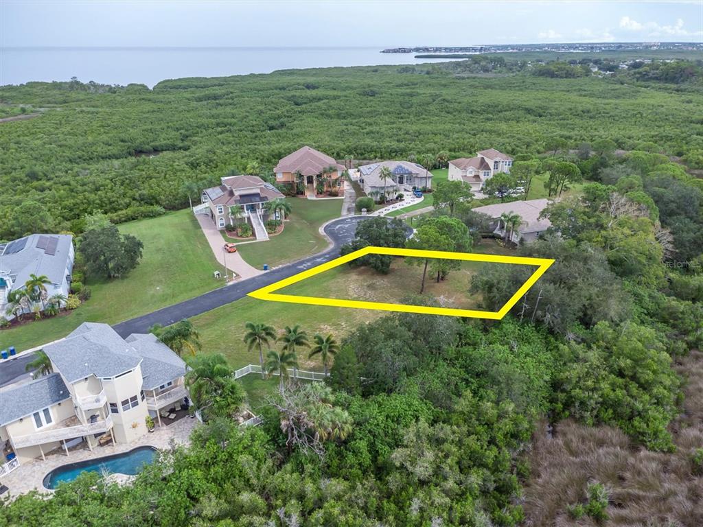 An aerial view shows a vacant residential lot outlined in yellow near a coastal forest — 3034 SHEPPARDS CROOK, HOLIDAY, FL