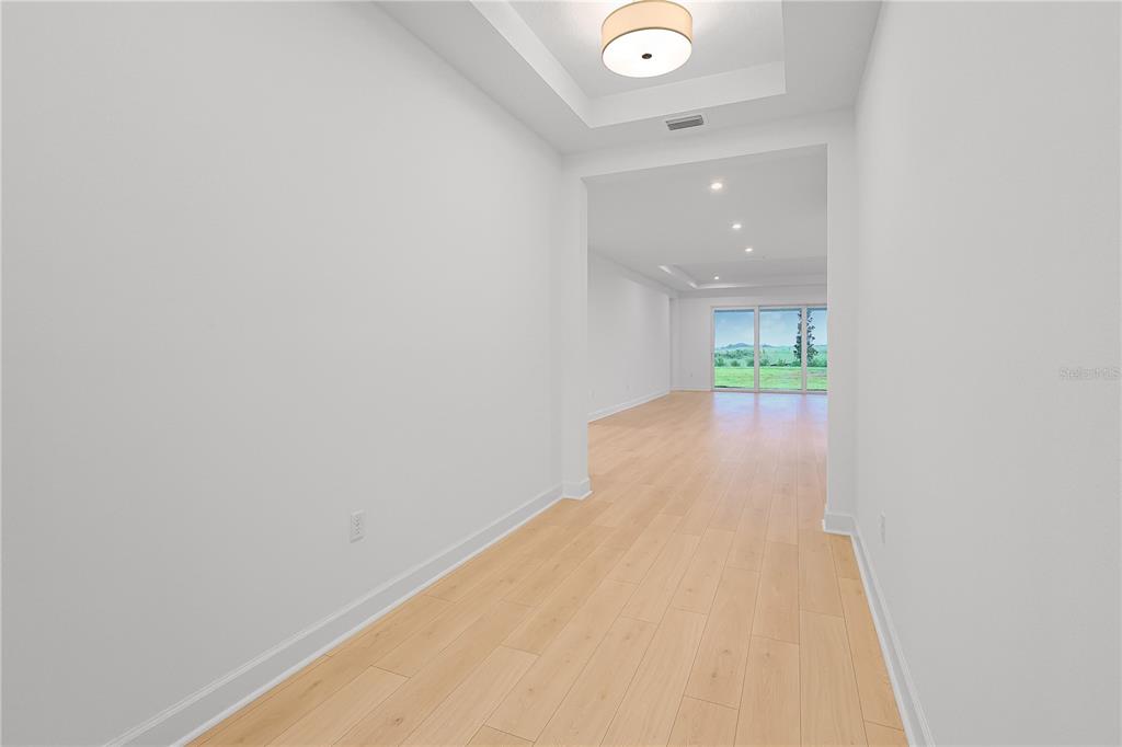 A bright hallway with light wood flooring leads into a spacious room with large windows — 1615 BELLAGIO LOOP, TAVARES, FL