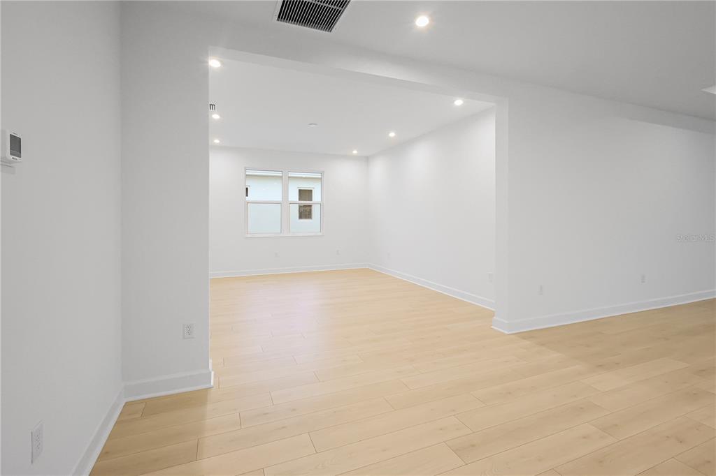 An empty room with light wood flooring and white walls features a recessed living area — 1615 BELLAGIO LOOP, TAVARES, FL