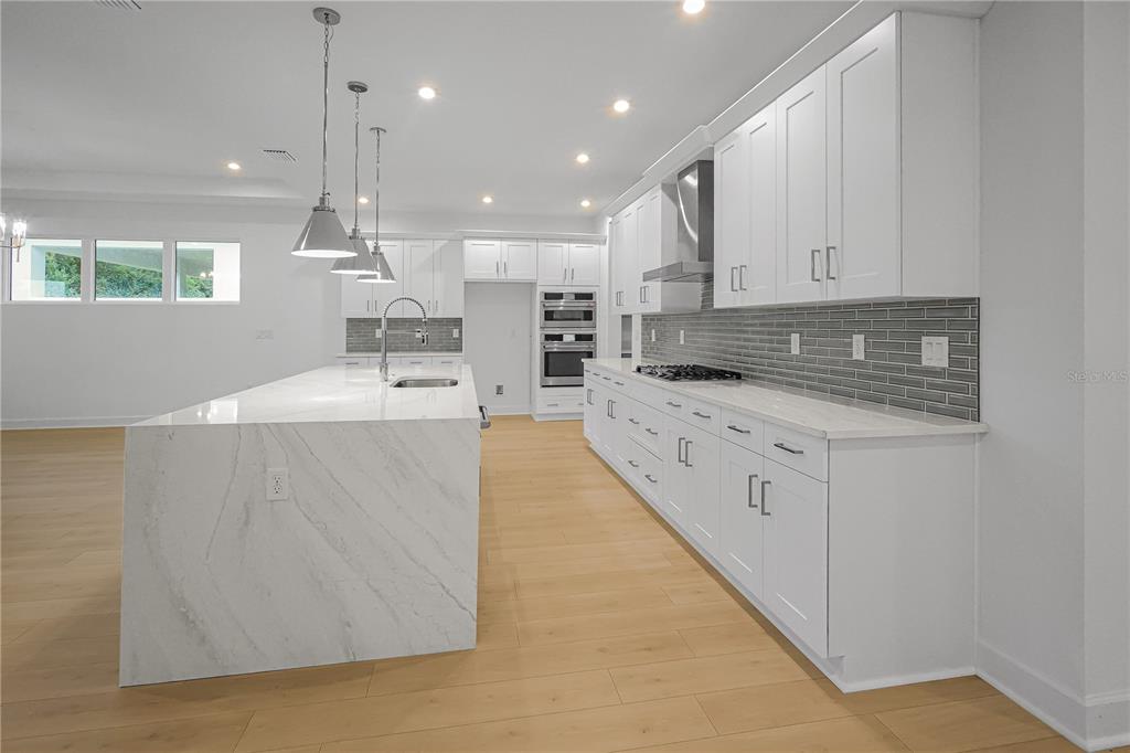 A modern kitchen features white cabinetry, a large marble-topped island, and gray subway tile backsplash — 1615 BELLAGIO LOOP, TAVARES, FL