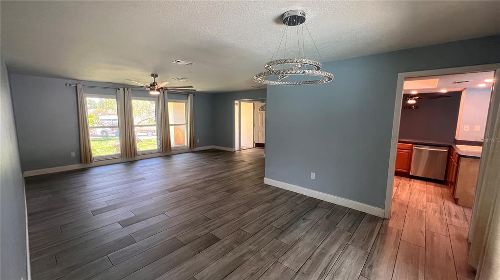 A living room with wood-look tile flooring, a modern chandelier, and an adjacent kitchen — 10007 LINDEN PLACE DRIVE, SEMINOLE, FL