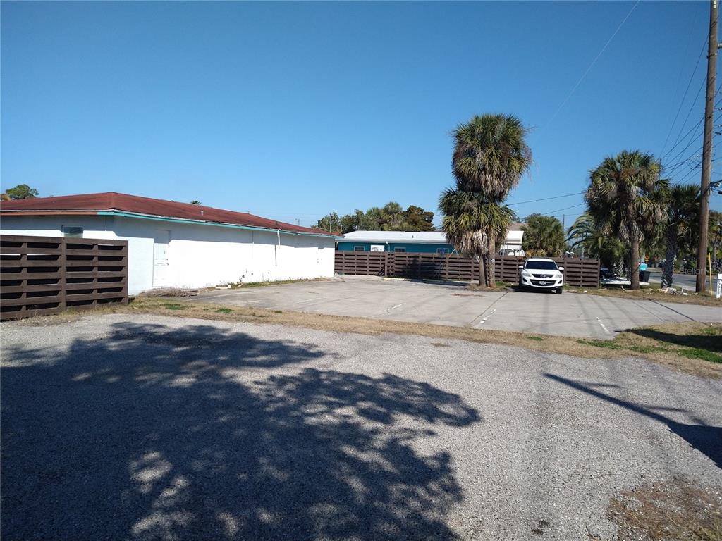 A gravel parking area leads to a concrete lot beside a white building with palm trees — 13923 OLD DIXIE HIGHWAY, HUDSON, FL