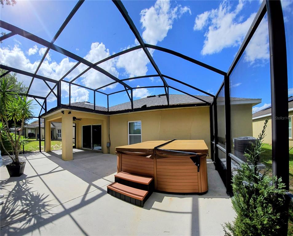 A screened-in patio features a hot tub with steps and a covered seating area — 316 ANDALUSIA LOOP, DAVENPORT, FL