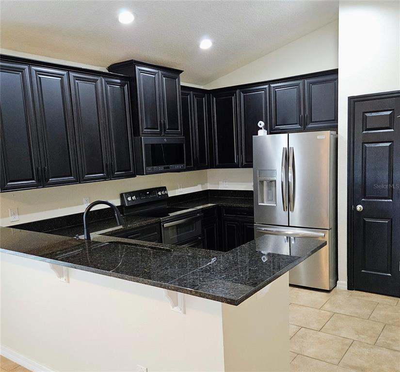 A kitchen features black cabinets, dark granite countertops, stainless steel appliances, and tile flooring — 316 ANDALUSIA LOOP, DAVENPORT, FL