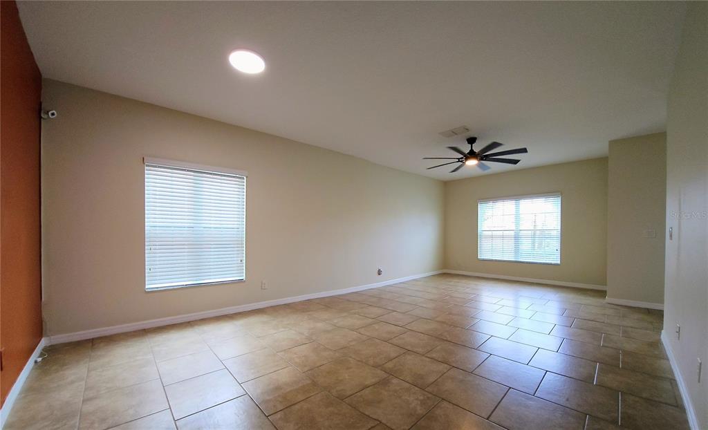 An empty living room features beige walls, tile flooring, a ceiling fan, and two windows — 316 ANDALUSIA LOOP, DAVENPORT, FL