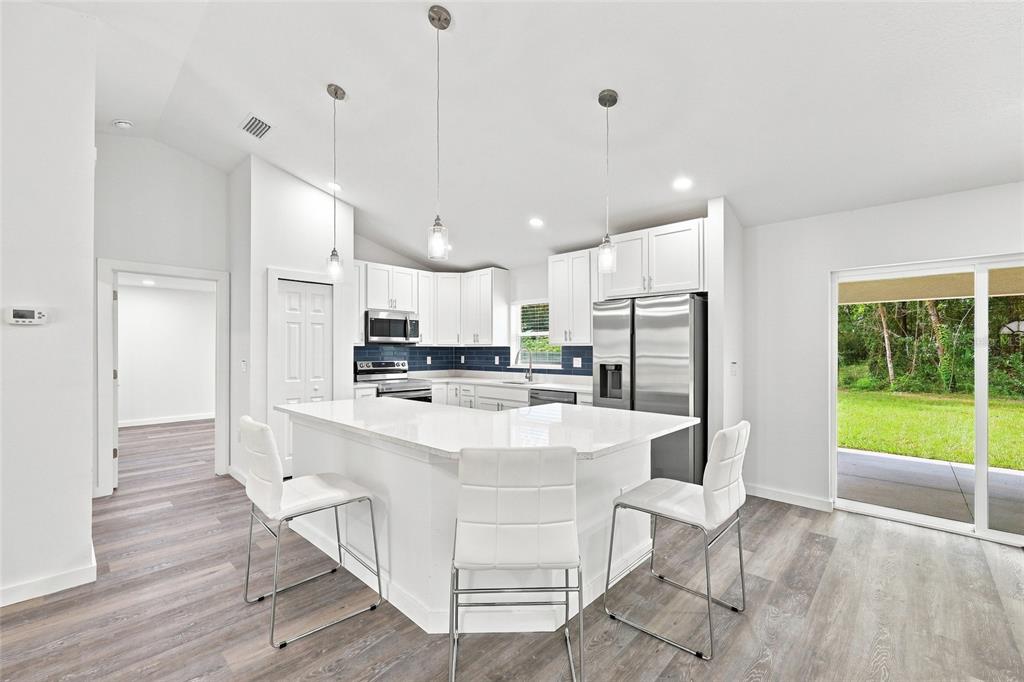 A modern kitchen features white cabinetry, a central island with bar seating, and stainless appliances — 2984 SE 140TH LANE, SUMMERFIELD, FL