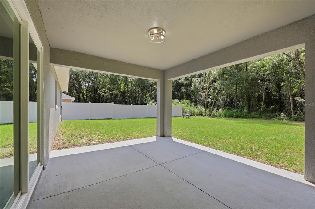 A covered concrete patio overlooks a grassy backyard enclosed by a white vinyl fence — 2984 SE 140TH LANE, SUMMERFIELD, FL