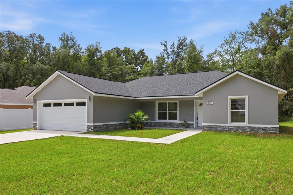 A single-story gray house with a white garage door, stone accents, and a front lawn — 2984 SE 140TH LANE, SUMMERFIELD, FL