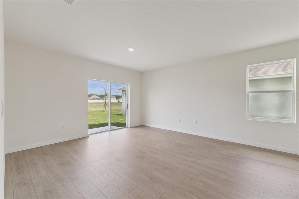 An empty room with light wood-look flooring, white walls, a sliding glass door, and window — 941 BLUET DRIVE, PORT ORANGE, FL