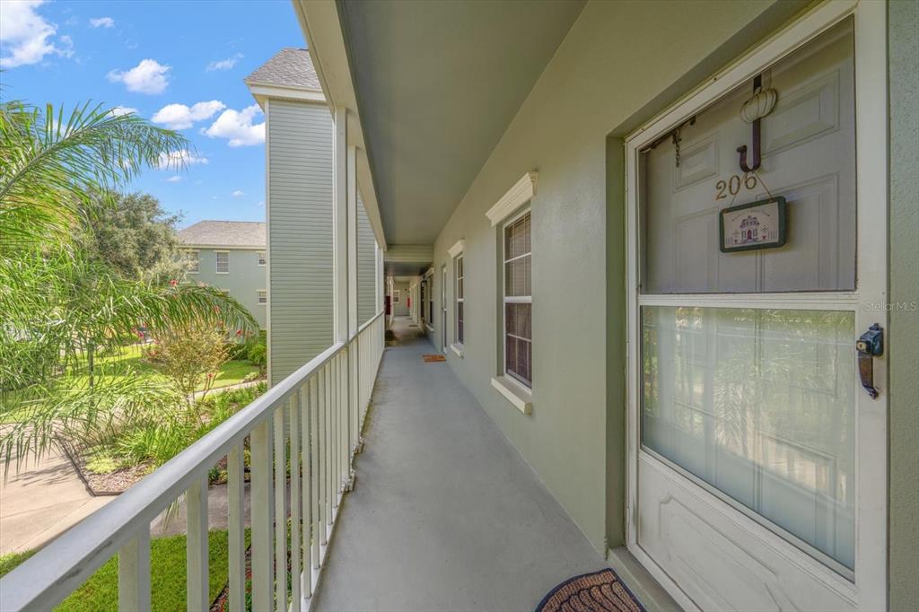 An outdoor apartment balcony features a white railing, light green walls, and a screen door — 330 PROMENADE DRIVE UNIT 206, DUNEDIN, FL