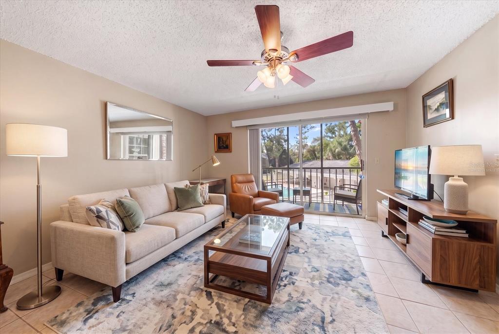 A living room features a beige sofa, glass coffee table, leather armchair, and sliding glass doors — 330 PROMENADE DRIVE UNIT 206, DUNEDIN, FL