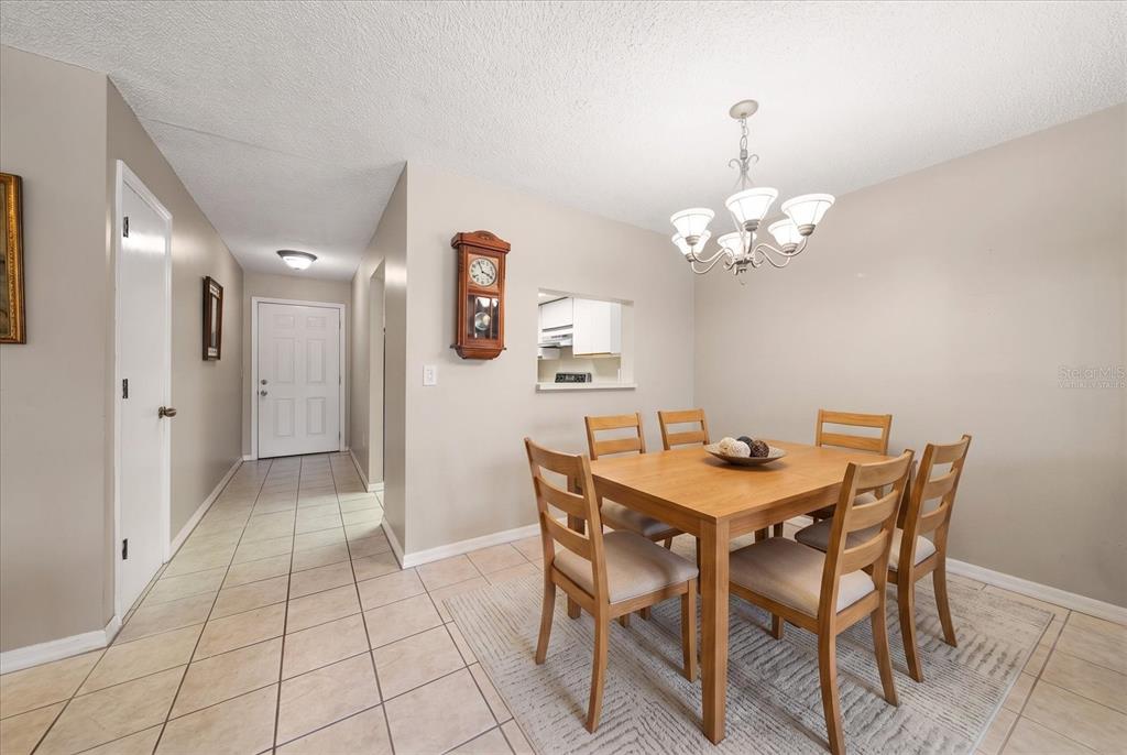 A dining area with a wooden table, four chairs, a chandelier, and tiled flooring — 330 PROMENADE DRIVE UNIT 206, DUNEDIN, FL