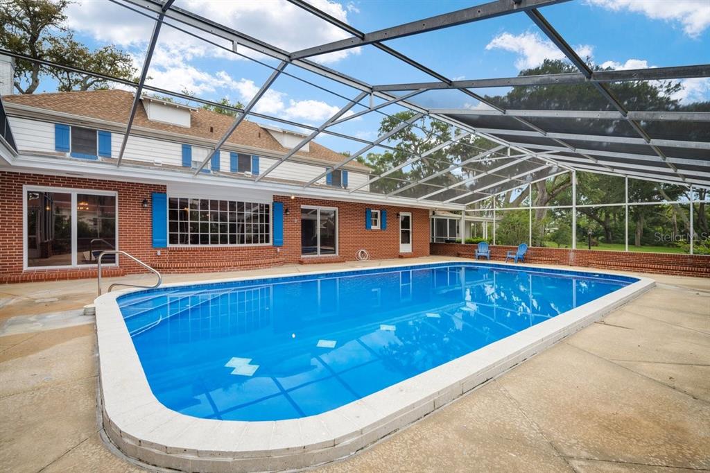 A rectangular swimming pool sits on a patio enclosed by a large metal screen cage — 639 & 659 JOHN ANDERSON DRIVE, ORMOND BEACH, FL
