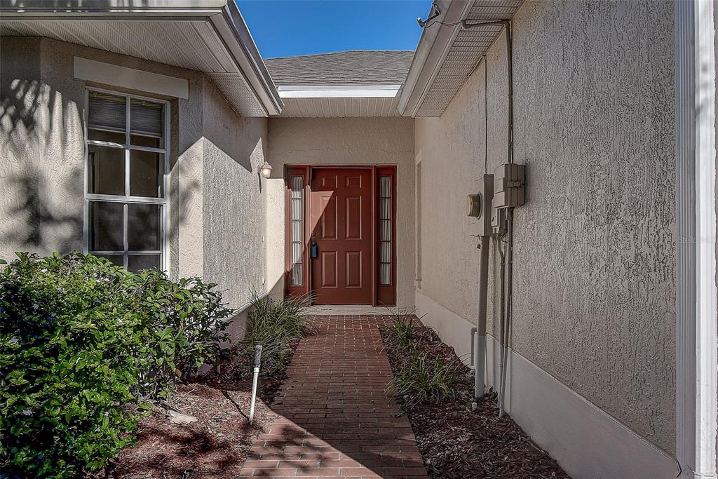 A brick walkway leads to a brown front door flanked by sidelights on a stucco house — 29417 CADDYSHACK LANE, SAN ANTONIO, FL