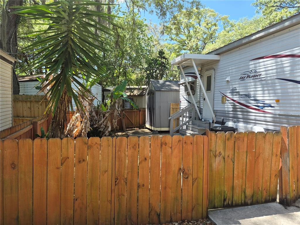 A wooden fence encloses a yard containing a travel trailer, a storage shed, and trees — 3000 CLARCONA ROAD UNIT 530, APOPKA, FL