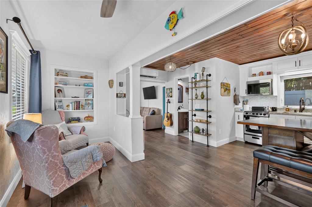 A living area with a patterned armchair, built-in shelving, and an open kitchen with wood-paneled ceilings — 4634 BIGLER LANE, MOUNT DORA, FL