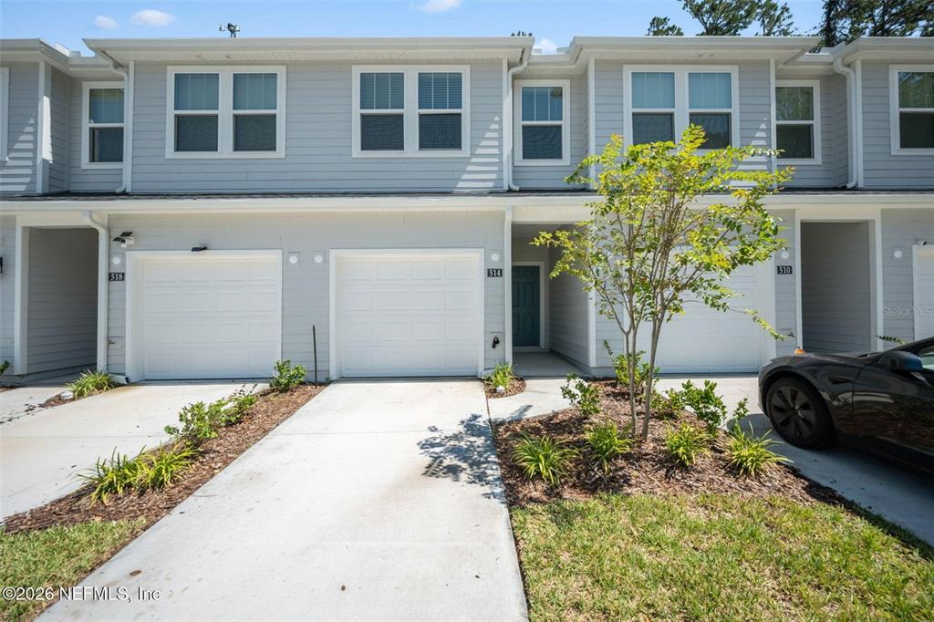 A row of light gray townhouses features white garage doors and a small front yard — 514 HOLLYLAKES DRIVE, ORANGE PARK, FL