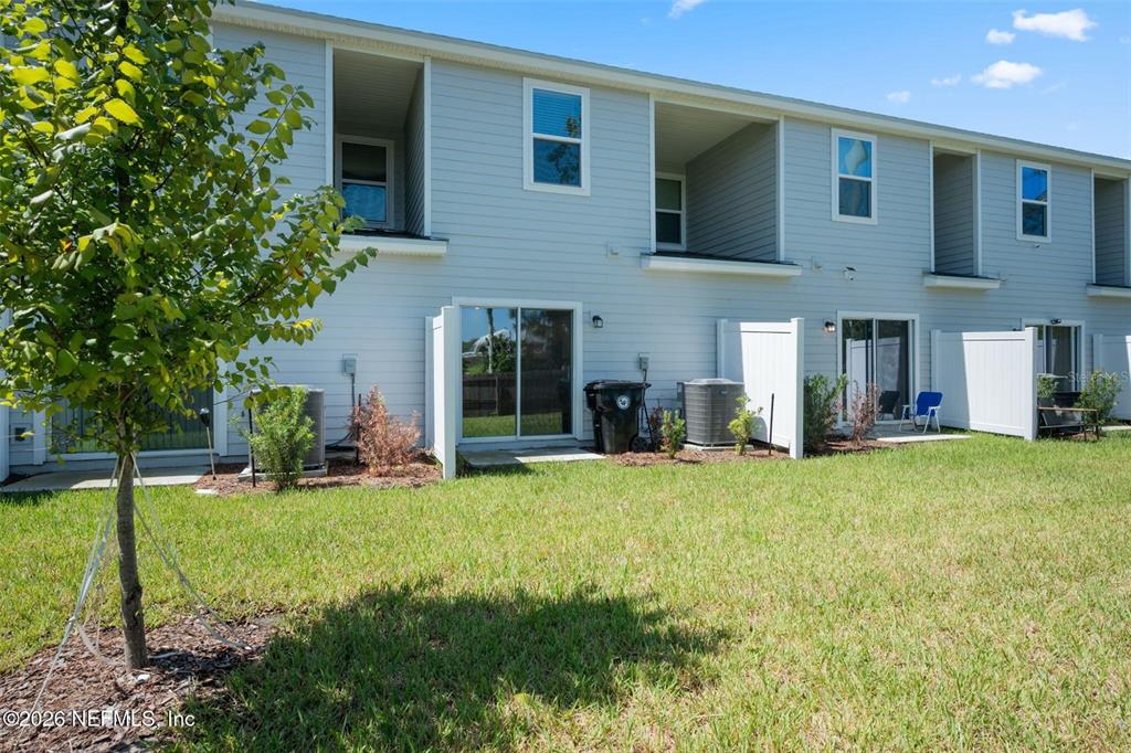 The rear exterior of a multi-unit townhouse features sliding glass doors and small private patios — 514 HOLLYLAKES DRIVE, ORANGE PARK, FL