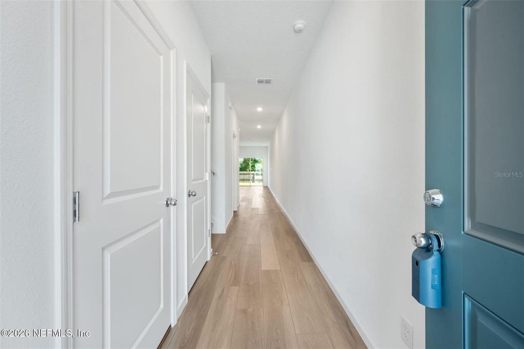 A long hallway with light wood flooring leads to a glass door at the end — 514 HOLLYLAKES DRIVE, ORANGE PARK, FL