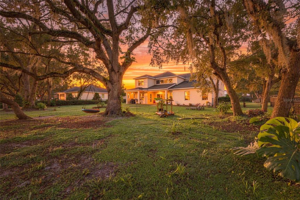 A two-story house with a large backyard, mature oak trees, and a sunset sky — 12754 SERONERA VALLEY COURT, SPRING HILL, FL