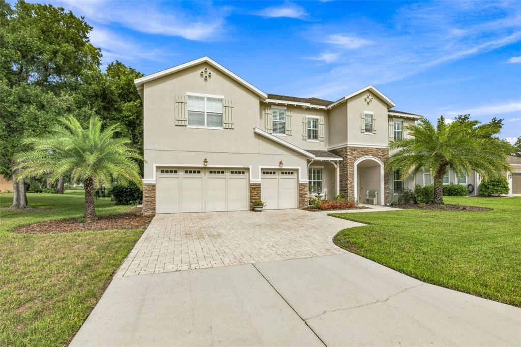 A two-story house with a three-car garage, stone accents, and palm trees in the yard — 12754 SERONERA VALLEY COURT, SPRING HILL, FL