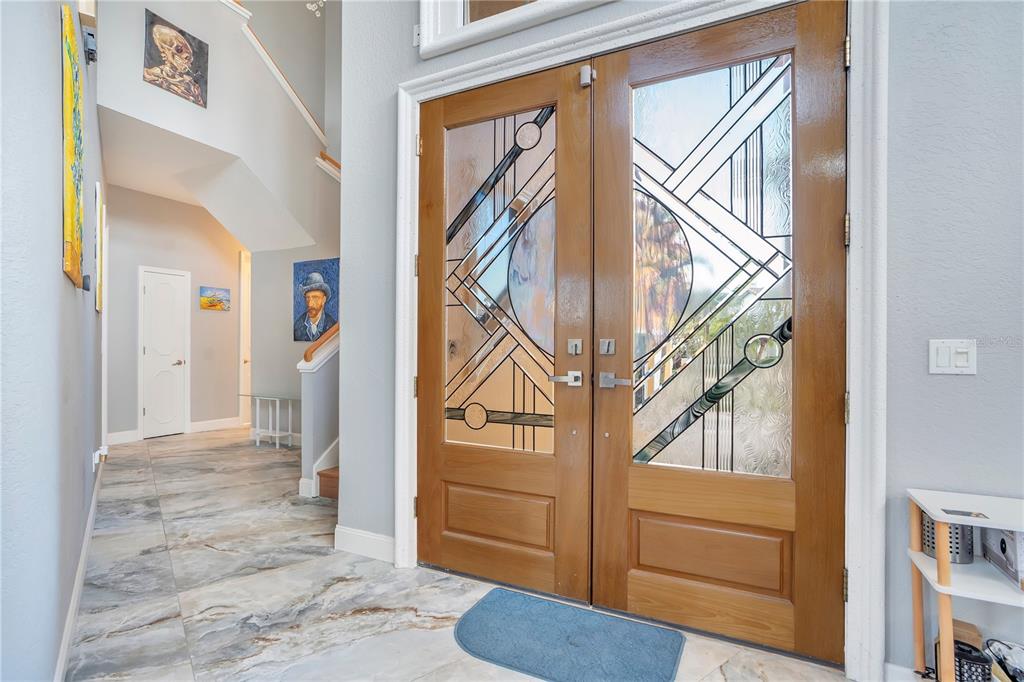 An entryway features double wood doors with geometric glass panels and marble-look tile flooring — 934 SYMPHONY ISLES BOULEVARD, APOLLO BEACH, FL