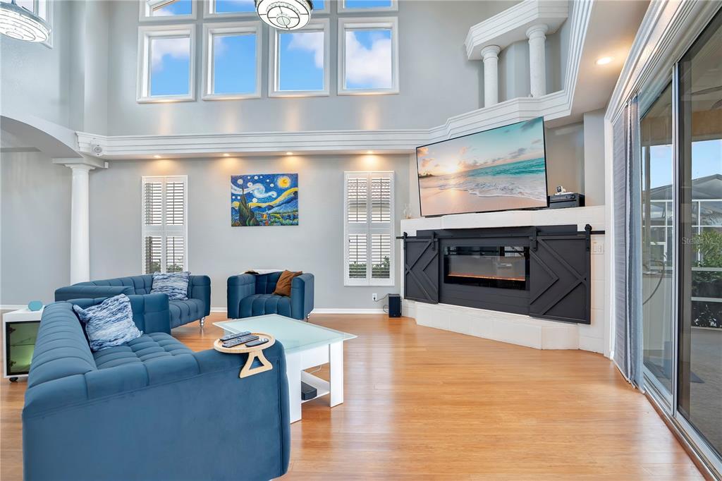 A living room features a blue sofa, a fireplace with sliding doors, and high windows — 934 SYMPHONY ISLES BOULEVARD, APOLLO BEACH, FL