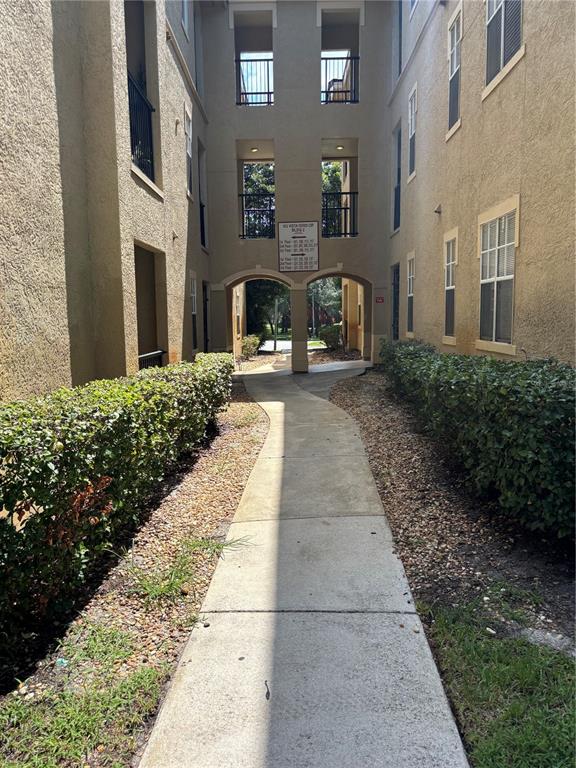 A concrete walkway leads between two tan apartment buildings with arched breezeways and landscaping — 103 VISTA VERDI CIRCLE UNIT 229, LAKE MARY, FL
