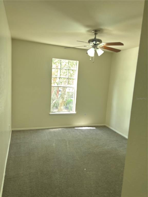 An empty bedroom features beige walls, gray carpeting, a ceiling fan, and a single window — 103 VISTA VERDI CIRCLE UNIT 229, LAKE MARY, FL