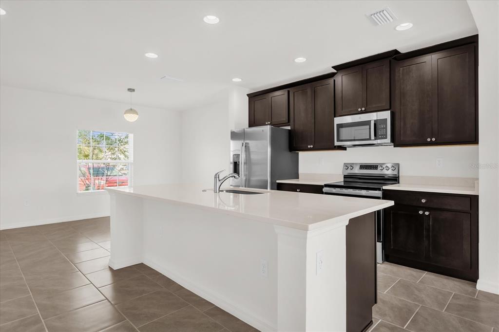 A kitchen features dark wood cabinets, stainless steel appliances, and a large white island — 1108 SAND TORCH CIRCLE, DAVENPORT, FL