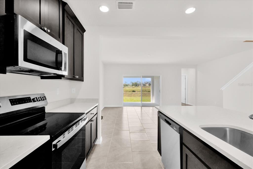 A kitchen with dark cabinets, white countertops, and stainless steel appliances overlooks a bright living area — 1108 SAND TORCH CIRCLE, DAVENPORT, FL