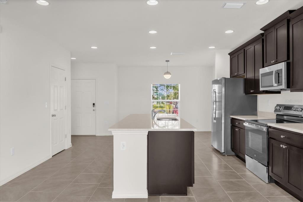 A kitchen features dark wood cabinets, stainless steel appliances, a quartz island, and tile flooring — 1108 SAND TORCH CIRCLE, DAVENPORT, FL