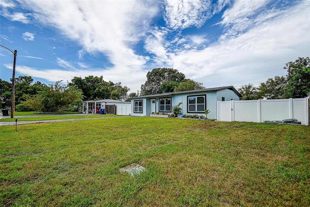 A light blue single-story house with a white vinyl fence and a large front lawn — 7580 MEADOWLAWN DRIVE N, ST PETERSBURG, FL
