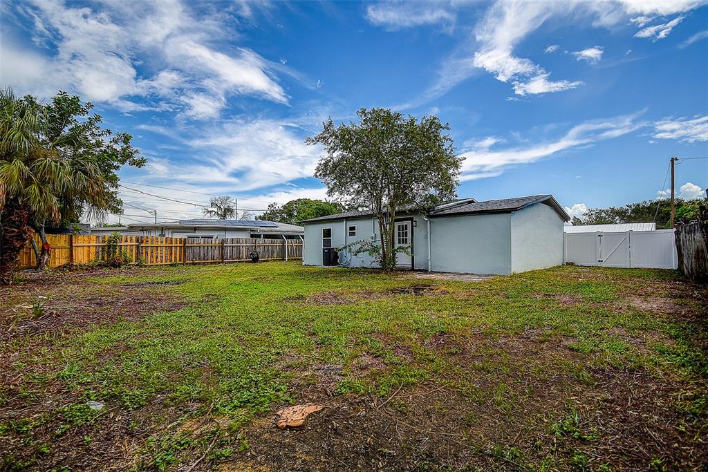 A backyard view of a light blue house with a tree and a wooden fence — 7580 MEADOWLAWN DRIVE N, ST PETERSBURG, FL