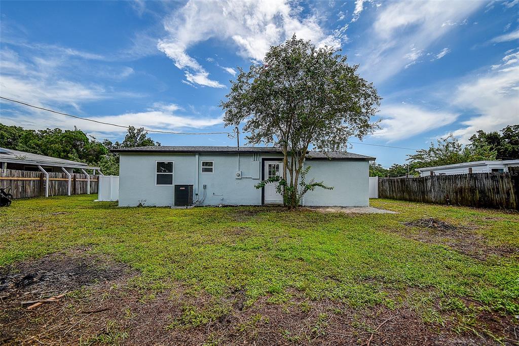 A light blue house exterior with a large tree in the backyard and wooden fencing — 7580 MEADOWLAWN DRIVE N, ST PETERSBURG, FL