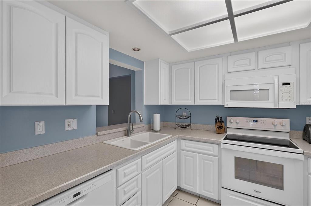 A kitchen features white cabinets, light countertops, a white appliance suite, and blue walls — 3167 LANDMARK DRIVE UNIT 821, CLEARWATER, FL