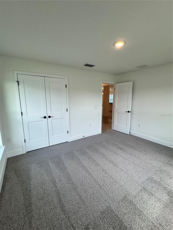 A bedroom with gray carpet, white walls, double closet doors, and an open doorway — 2659 AVERLAND LOOP, NORTH PORT, FL