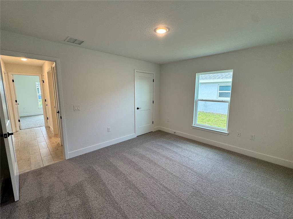 A carpeted bedroom features white walls, a single window, and a doorway leading to a hallway — 2659 AVERLAND LOOP, NORTH PORT, FL