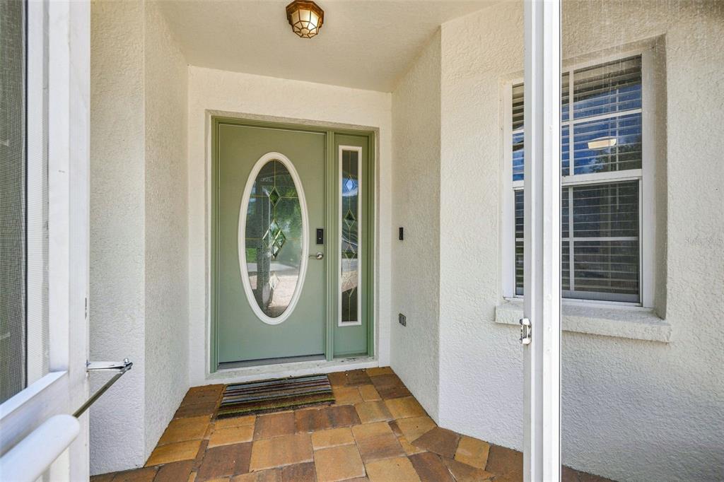 A sage green front door with a glass oval insert sits on a tiled porch — 10345 COLLAR DRIVE, SAN ANTONIO, FL