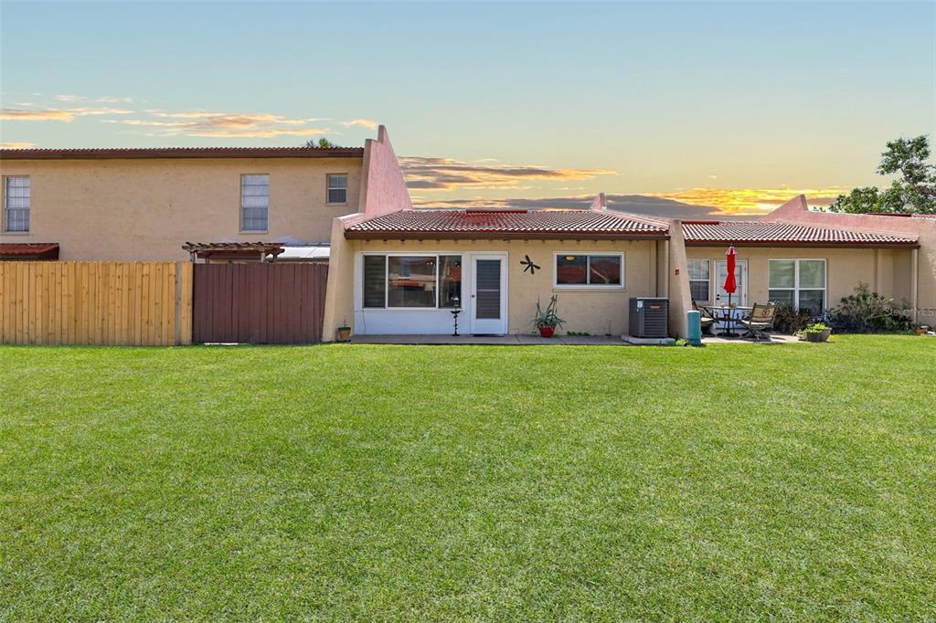 The exterior view shows the back of a tan townhouse with a large grassy yard — 7200 ULMERTON ROAD UNIT E3, LARGO, FL