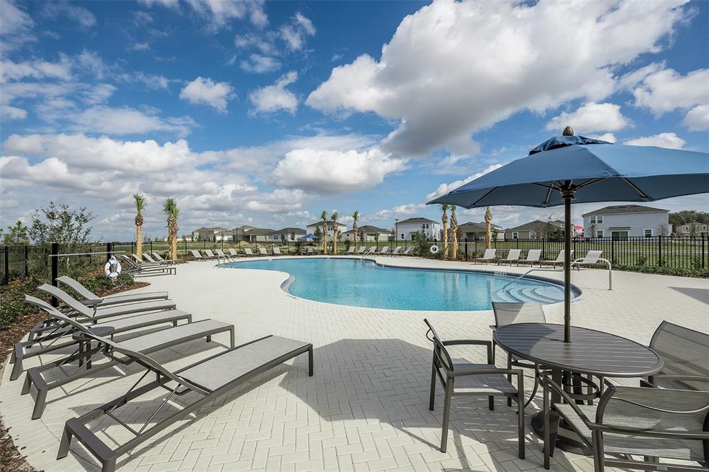 A swimming pool with lounge chairs and a patio table sits under a blue sky — 7409 FIELDSTONE DRIVE, GROVELAND, FL