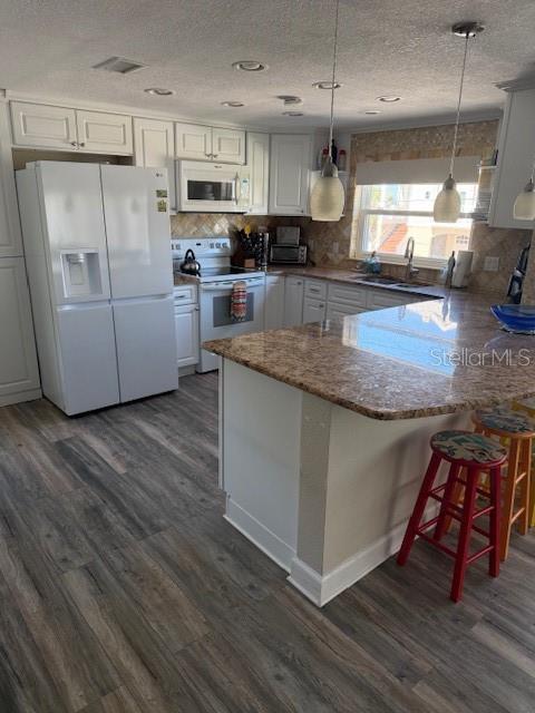 A kitchen features white cabinets, a white refrigerator, a granite island, and wood-look flooring — 745 ELDORADO AVENUE, CLEARWATER BEACH, FL