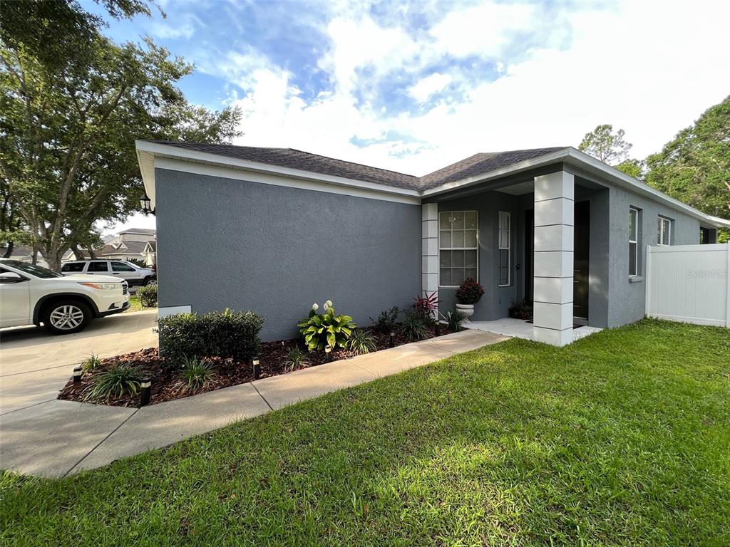 A gray stucco house features a concrete walkway leading to a covered front entryway — 6138 KITERIDGE DRIVE, LITHIA, FL
