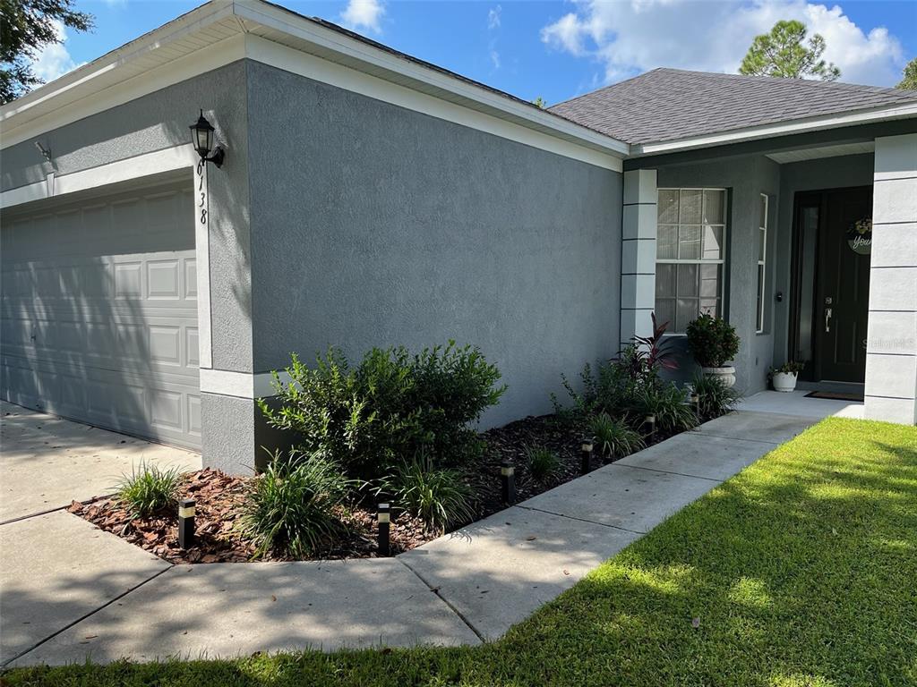 A gray stucco house exterior features a garage, a front walkway, and landscaped garden beds — 6138 KITERIDGE DRIVE, LITHIA, FL