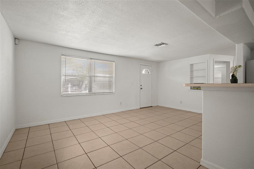 An empty living room with white walls, tile flooring, a window with blinds, and a door — 3438 KIMBERLY OAKS DRIVE, HOLIDAY, FL