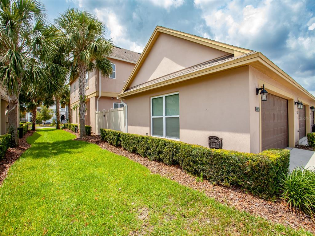 A side view of a tan house with a garage, a window, and manicured landscaping — 11734 WATER RUN ALLEY, WINDERMERE, FL