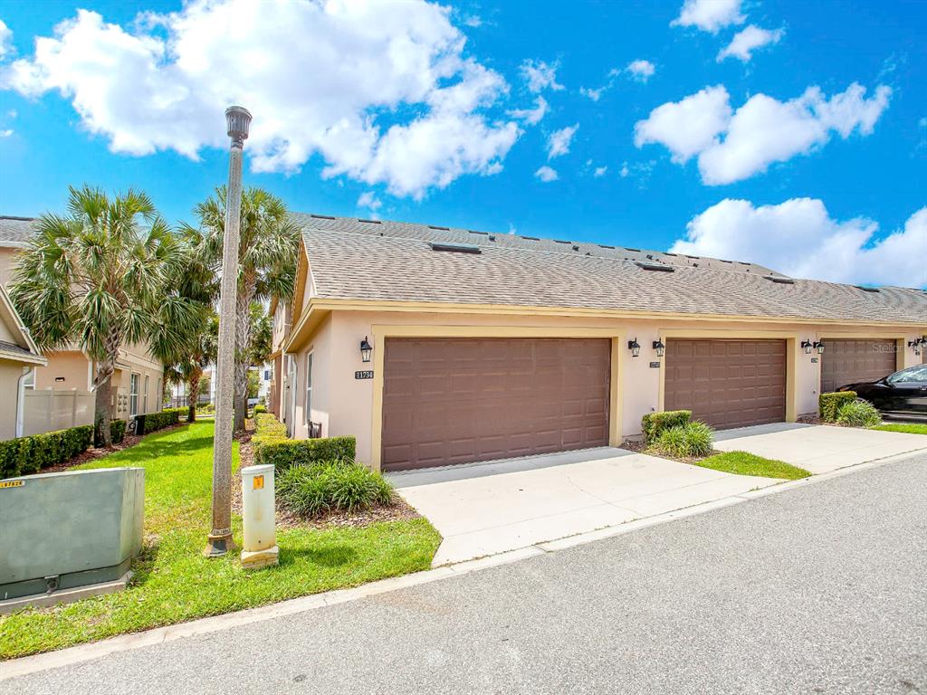 A tan townhome exterior features two brown garage doors and a small patch of lawn — 11734 WATER RUN ALLEY, WINDERMERE, FL