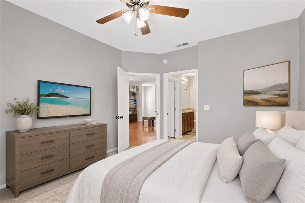 A bedroom with a dresser, wall-mounted television, ceiling fan, and an attached bathroom doorway — 114 VISTA VERDI CIRCLE UNIT 216, LAKE MARY, FL