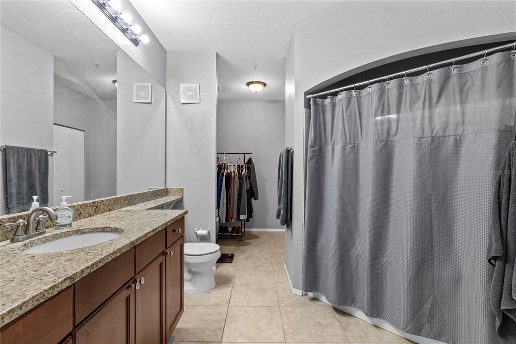 A bathroom features a granite vanity, a toilet, and a shower with a gray curtain — 114 VISTA VERDI CIRCLE UNIT 216, LAKE MARY, FL